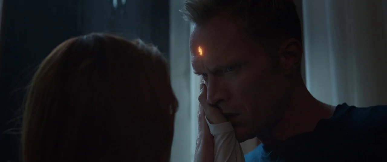 Avengers: Infinity War (2018) movie still: medium — An interior space with a dimly lit setting and shadows. A woman touches a man's face while a…