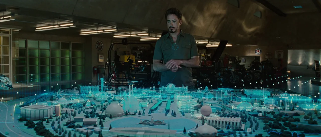 Iron Man 2 (2010) movie still: medium — A spacious workshop filled with industrial equipment and a large central table. A man in a green shirt…