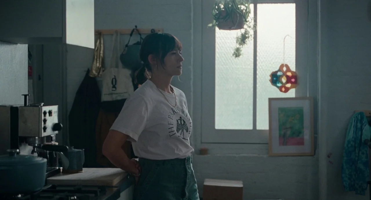 On The Rocks (2020) movie still: medium — A residential space with white painted brick walls and a window with hanging plants. A woman in a white…