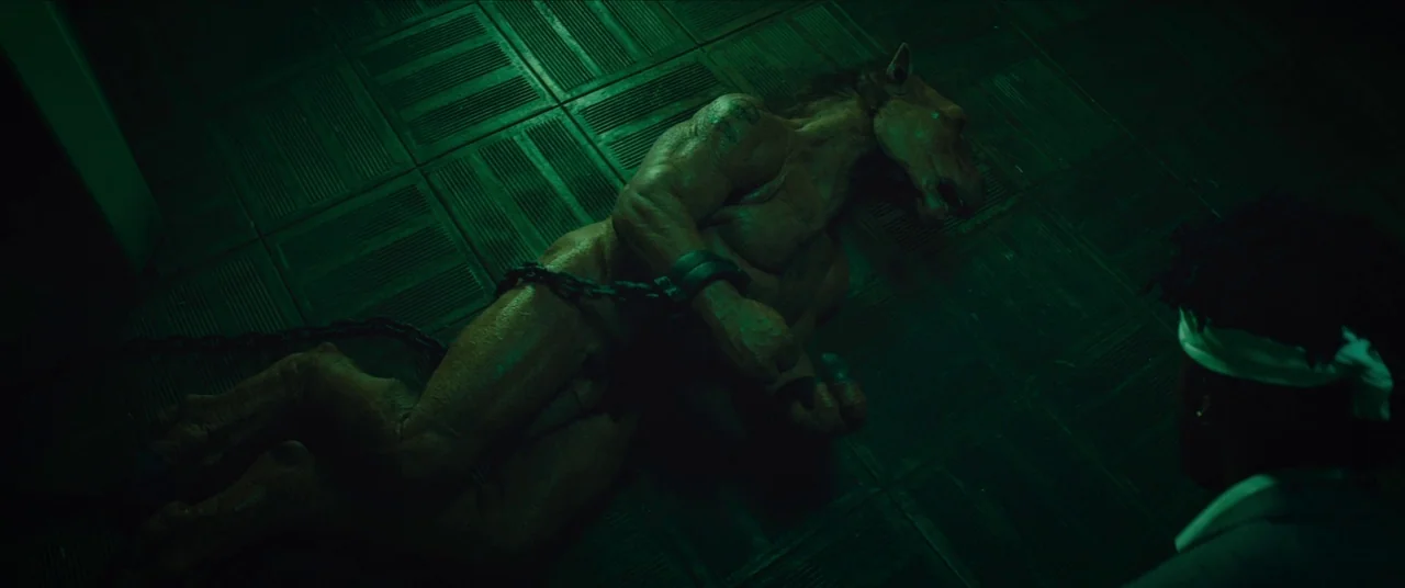 Sorry to Bother You (2018) movie still: medium — A dimly lit room with a tiled floor under harsh green illumination. A muscular horse-headed hybrid…