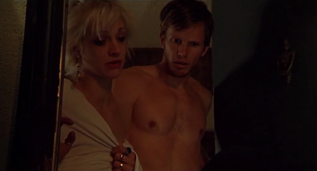 The Heart Is Deceitful Above All Things (2004) movie still: medium — A dimly lit narrow hallway with shadowed walls. A woman and a shirtless man…