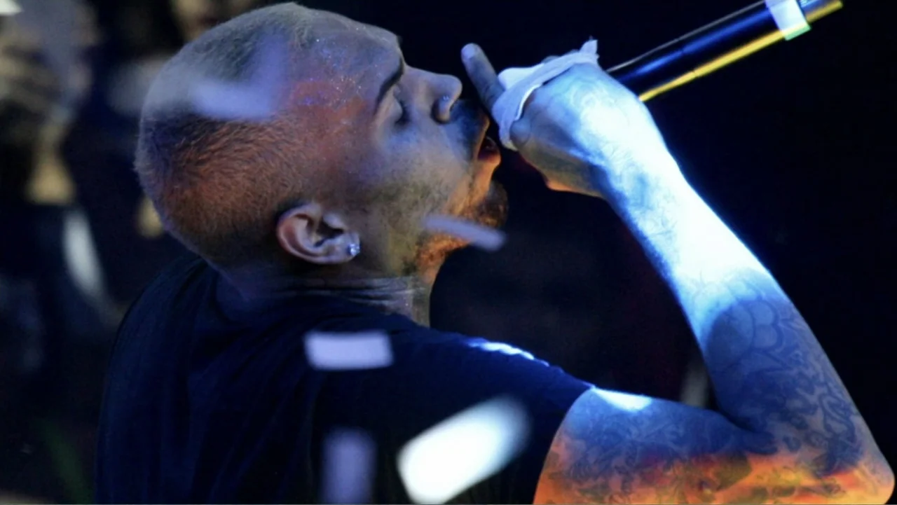 Chris Brown: A History of Violence (2024) movie still: medium — A dark concert stage environment with blurred white confetti floating in the…