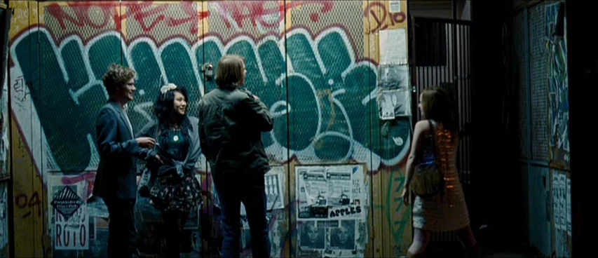 This Movie Is Broken (2010) movie still: wide — An urban alleyway features a metal rolling shutter covered with dark green graffiti layers. Four…
