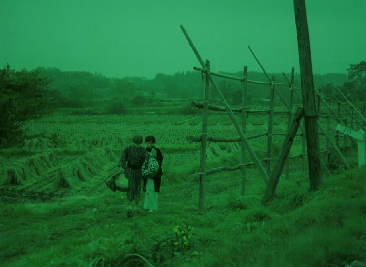 Pastoral To Die In The Country (1974) movie still: wide — A rural farmland with bundled hay and a tall wooden frame structure. Two figures walk…