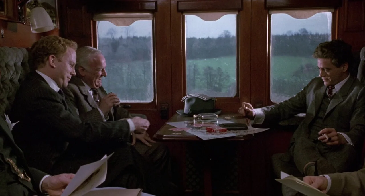 Chaplin (1992) movie still: medium — A wooden train compartment with tall windows looks out over a green rural landscape. Three men in suits sit…