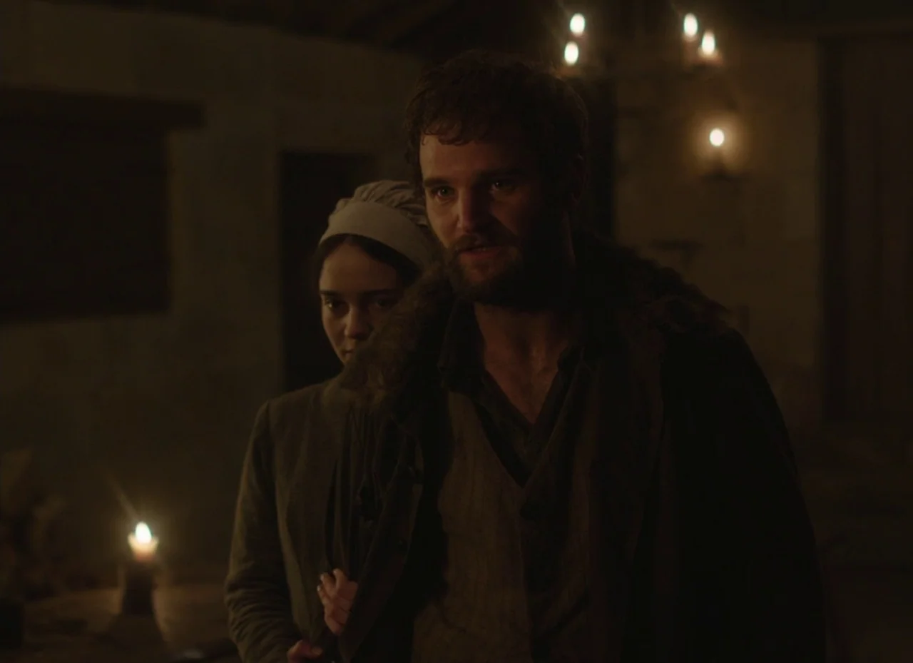 The Nightingale (2018) movie still: medium — A dimly lit room with stone or wood walls features flickering candles in the background. A man stands…