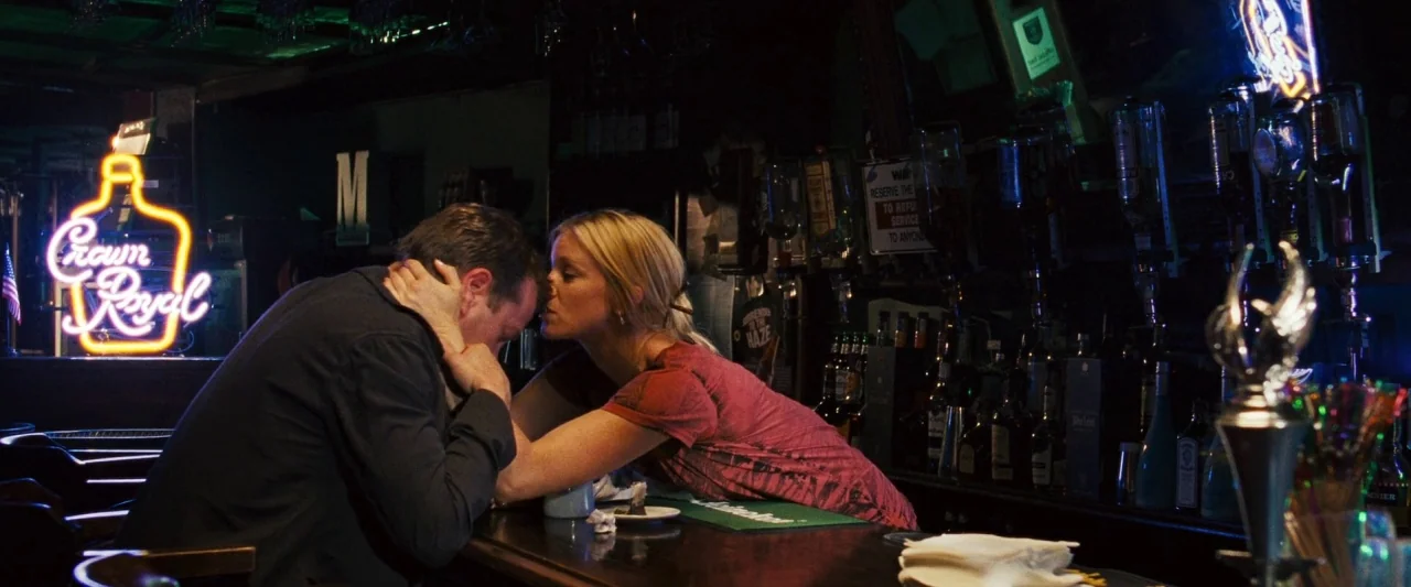 Mirrors (2008) movie still: medium — A dimly lit bar with a glowing Crown Royal neon sign in the background. A woman reaches across the wooden…