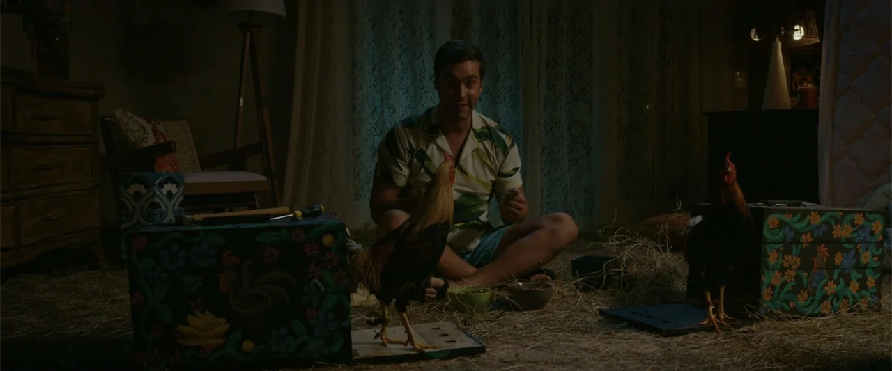 Beautiful Wedding (2024) movie still: medium — A dark indoor space is filled with loose straw and decorated wooden boxes. A man sits on the floor…