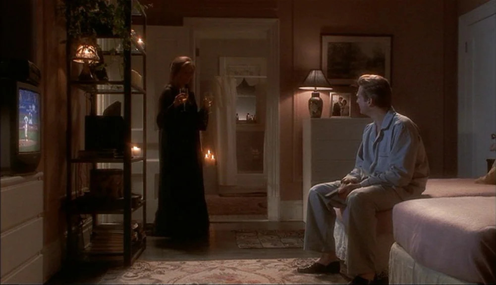 The Mirror Has Two Faces (1996) movie still: wide — A dimly lit bedroom features a television displaying a baseball game and a shelving unit. A man…