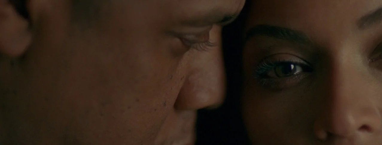 Lemonade (2016) movie still: closeup — A close-up view shows two faces positioned closely together in a dark space. The frame highlights the eyes…