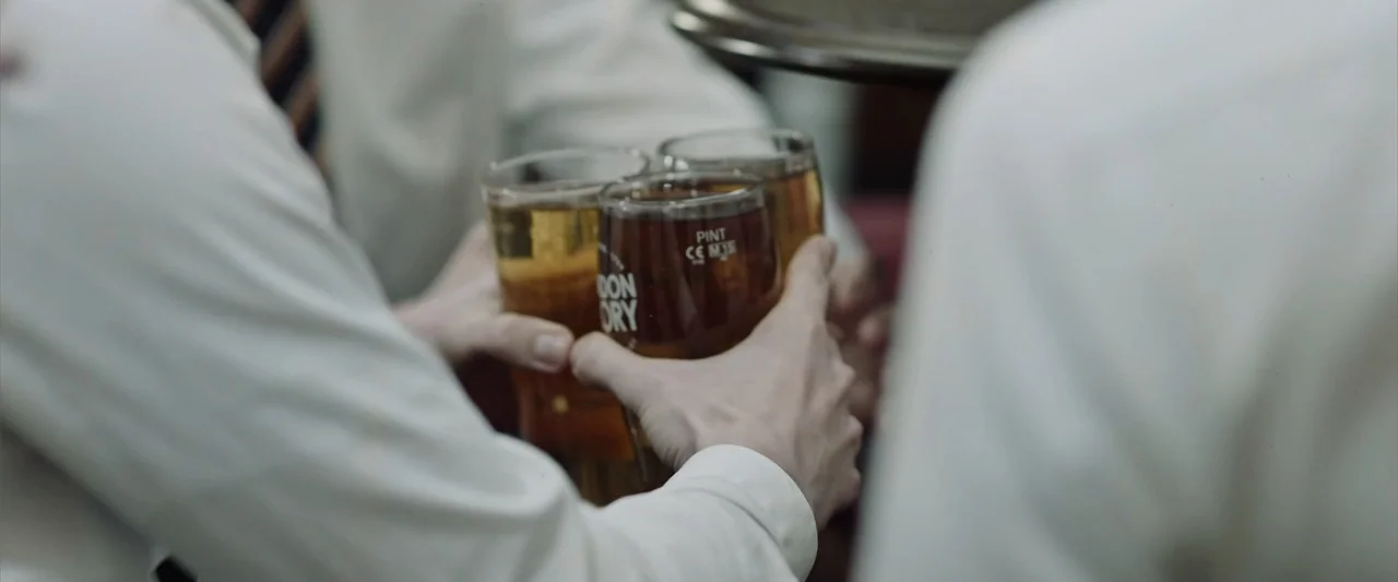 The Thorn On His Side (2014) movie still: medium — A group of people wearing white dress shirts gather in a dimly lit bar. The subjects hold three…