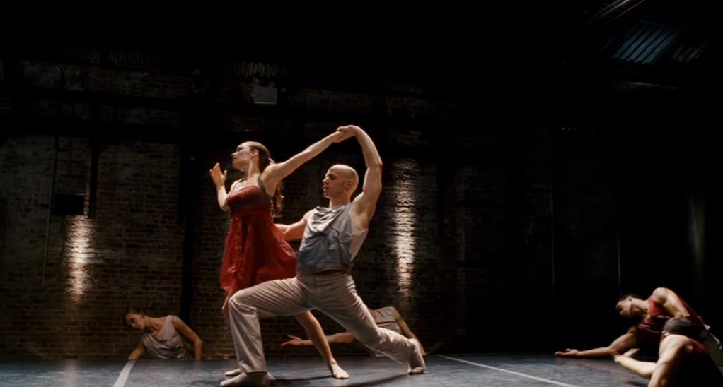 The Adjustment Bureau (2013) movie still: fullbody — A dark, dimly lit dance studio features an exposed brick wall background. A male dancer and a…