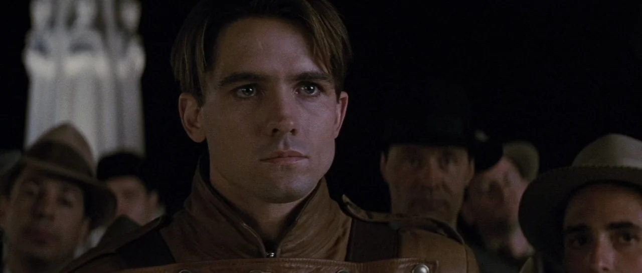 The Rocketeer (1991) movie still: closeup — A man stands amidst a gathering of people in a dark outdoor space at night. In the background a tall…