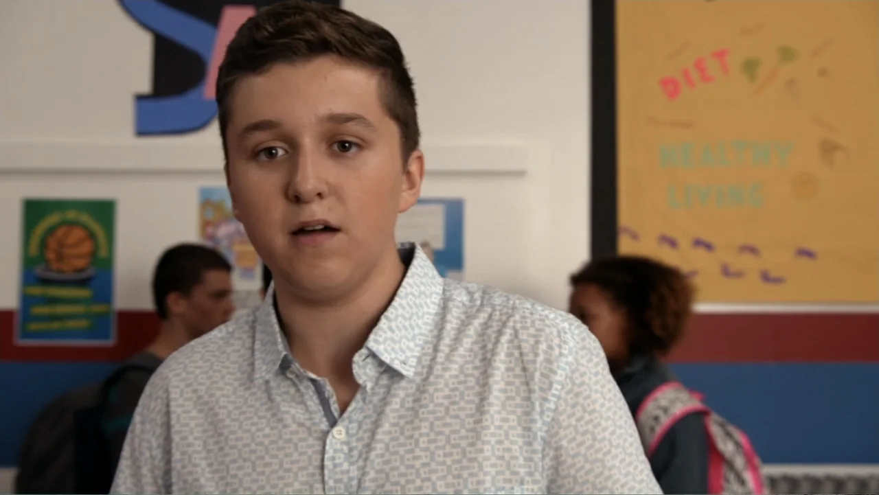Rufus 2 (2017) movie still: medium — A bright classroom wall features posters about healthy living and a basketball court graphic. A young male…