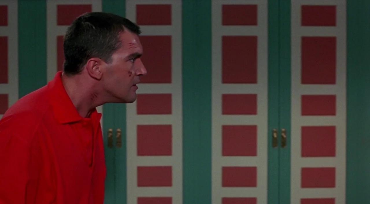 Tie Me Up! Tie Me Down! (1989) movie still: medium — A man stands in an interior corridor with decorative red and green paneled walls. The man has…