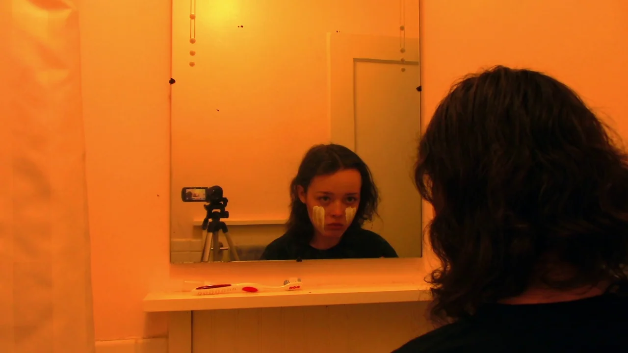 We’re All Going to the World’s Fair (2021) movie still: medium — A small bathroom with a rectangular mirror and a single white shelf underneath. A…