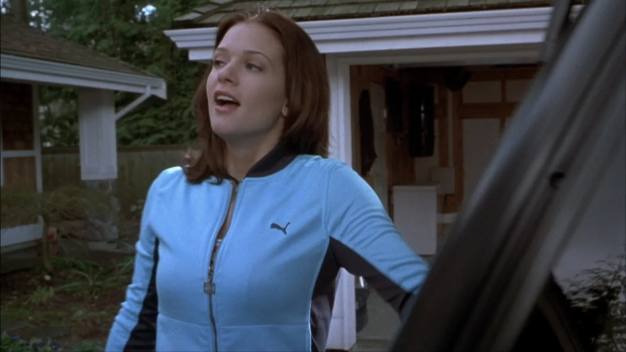 Final Destination 2 (2003) movie still: medium — A residential driveway with a white house garage visible in the background. A young woman in a blue…