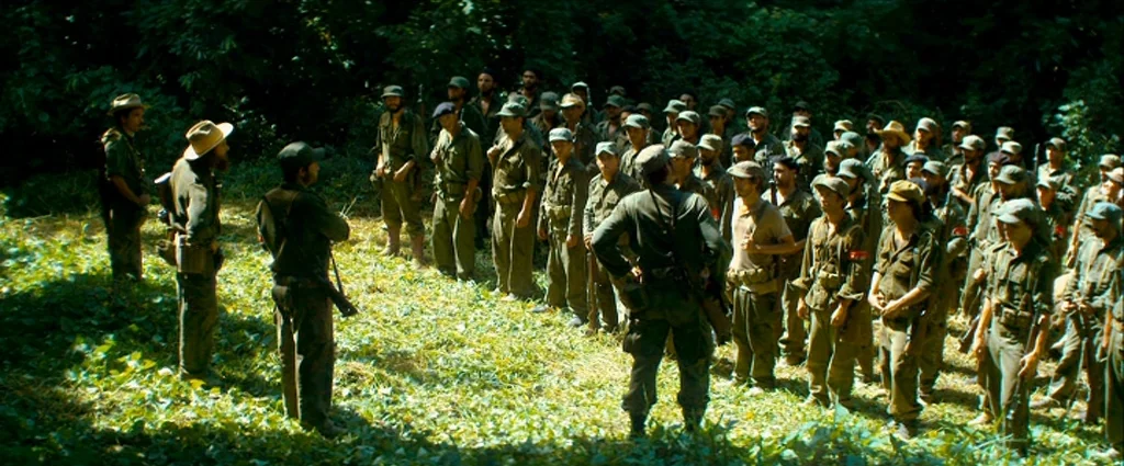 Che Part 1 (The Argentine) (2008) movie still: wide — A clearing within a dense tropical jungle serves as a gathering point for soldiers. A large…