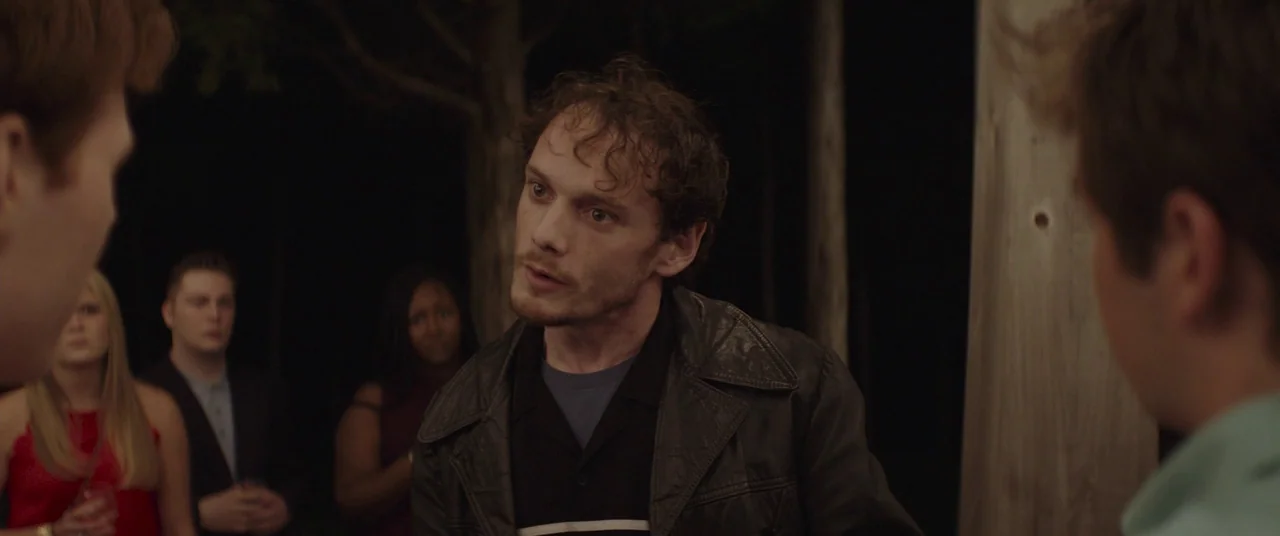 Thoroughbreds (2017) movie still: medium — An outdoor space at night with dark trees visible behind a group of people. A man in a leather jacket…