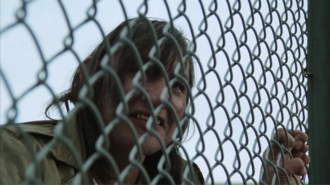 One Flew Over the Cuckoo's Nest (1975) movie still: closeup — A person stands behind a metal chain link fence in an outdoor setting. The subject…