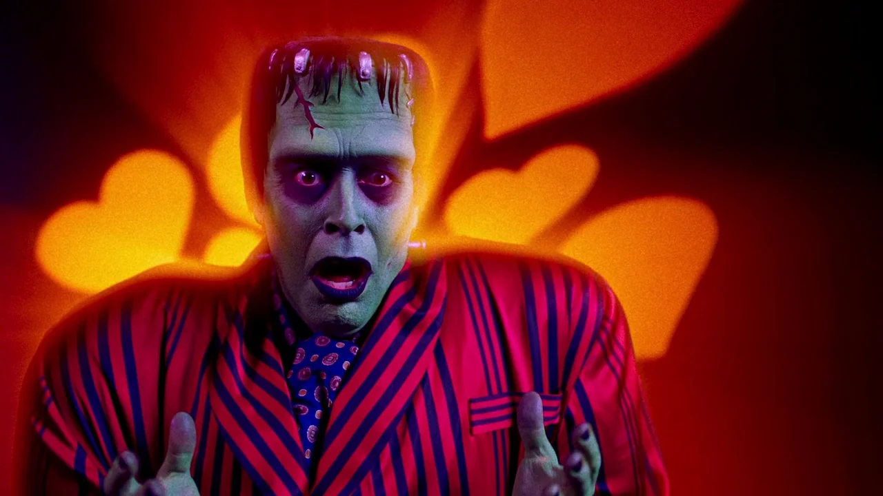 The Munsters (2022) movie still: closeup — A theatrical stage backdrop displays large luminous heart shapes in warm orange and yellow. The…