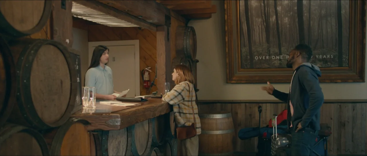 We Broke Up (2021) movie still: medium — A reception area features wooden barrels and a large nature photograph on the wall. Three people stand at a…