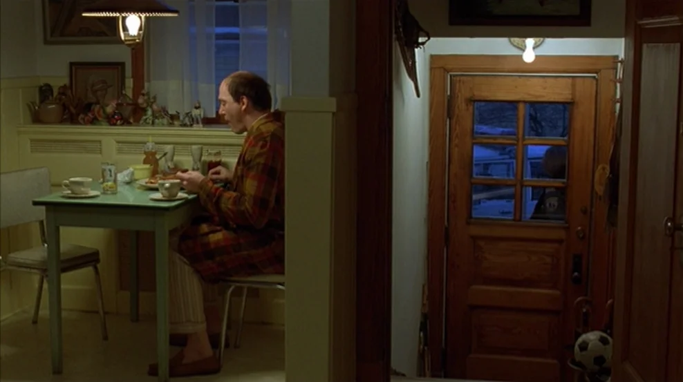 Fargo (1996) movie still: medium — A small dining nook features yellow wainscoting and a light green table next to a wooden door. A man sits at the…