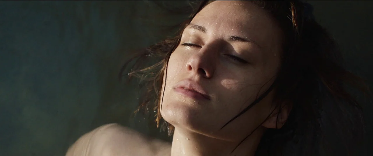 Nightsiren (2022) movie still: closeup — A woman's face floats at the surface of dark, rippling water. Her head is tilted back with eyes closed and…