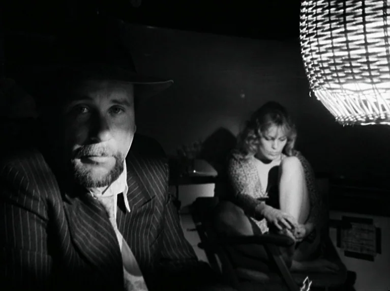 The American Soldier (1970) movie still: medium — A dimly lit interior room features a man in the foreground and woman behind. A woven lampshade…