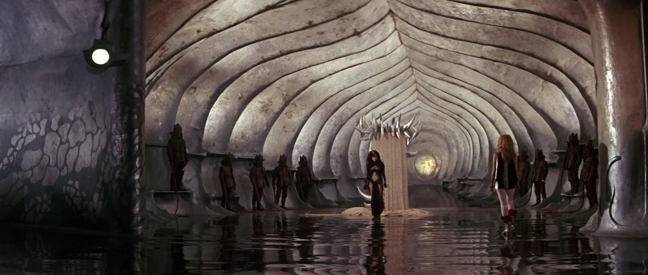 Barbarella (1968) movie still: wide — A vast vaulted hall with ribbed walls resembles the inside of a massive skeleton. Two women stand on a flooded…