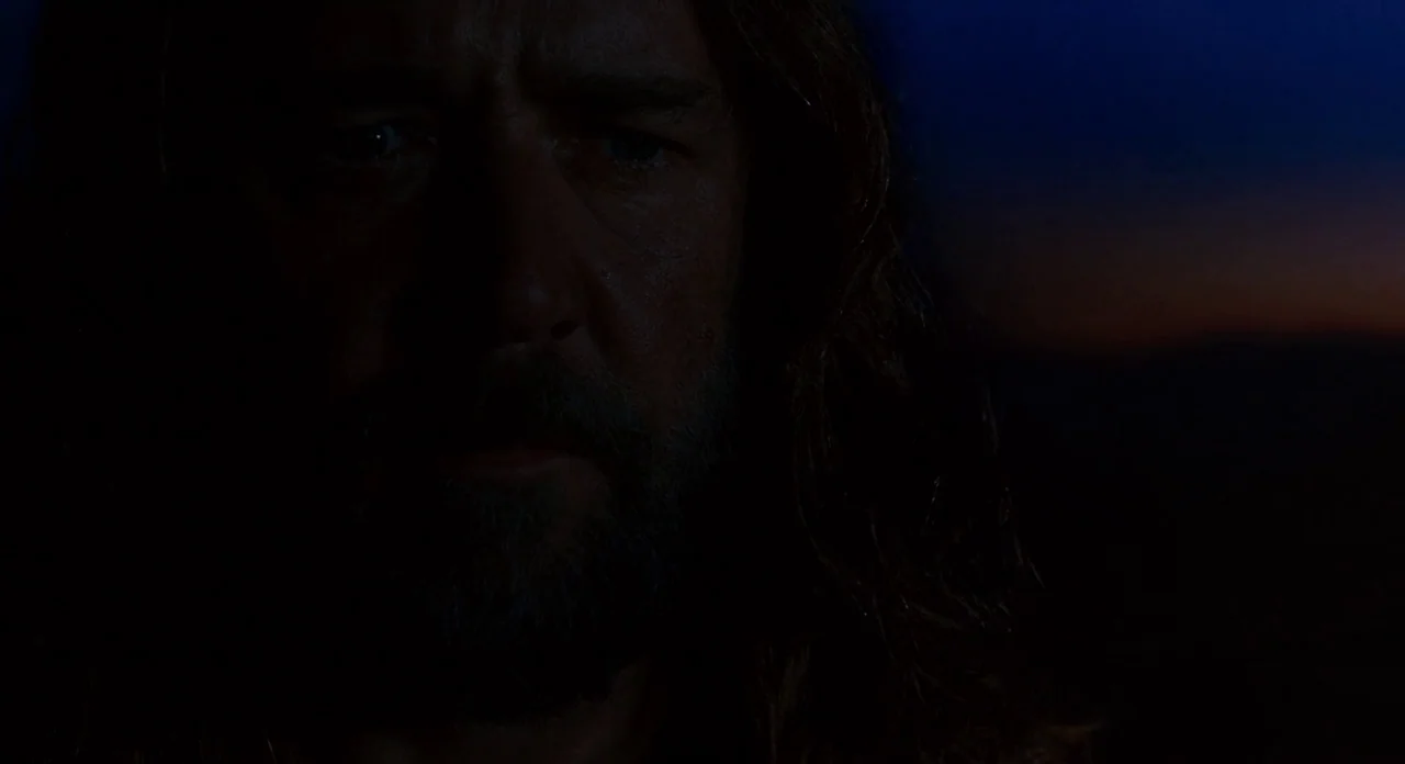 Noah (2014) movie still: closeup — A man's face appears in darkness against a dark blue evening sky. He looks forward with his face partially lit in…