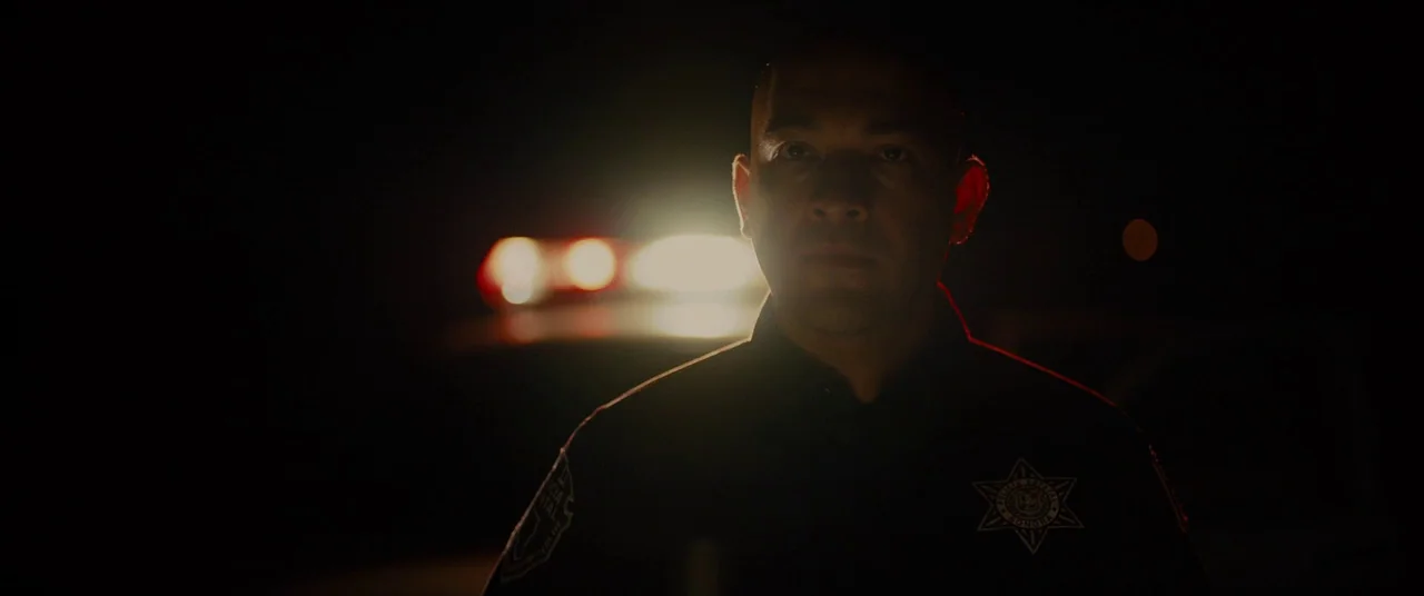 Sicario (2015) movie still: medium — A dark, unlit road at night with the silhouette of an officer visible. The officer stands directly in front of…