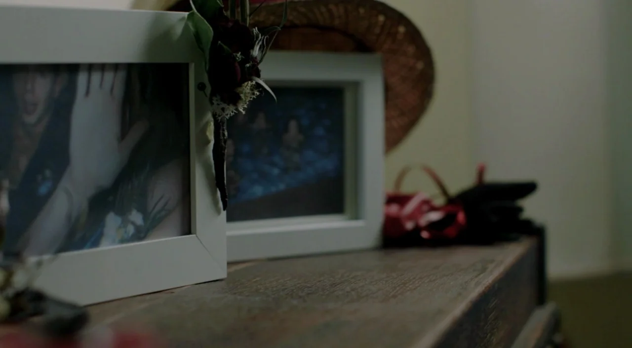 Laggies (2014) movie still: closeup — A wooden dresser top holds two white picture frames and a woven hat. A dried floral corsage hangs from the…