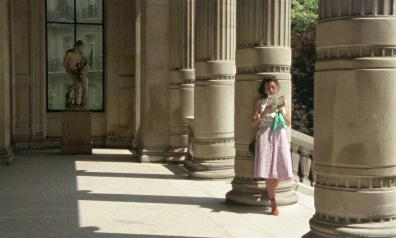 The Green Ray (1986) movie still: wide — A sunlit stone colonnade features large fluted columns and a sculpture standing behind glass. A young woman…