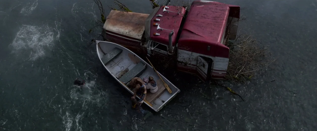Bird Box (2018) movie still: wide — A dark, fast-moving river contains the partially submerged cab of a large semi-truck. A small aluminum boat…