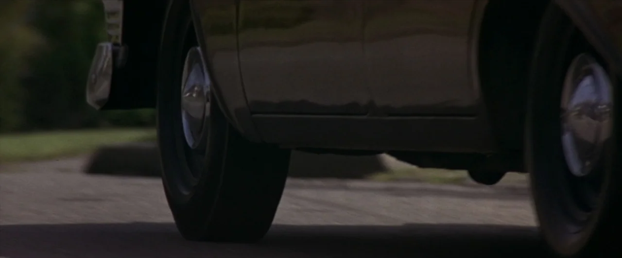 This Boy's Life (1993) movie still: closeup — An asphalt road surface extends across the lower portion of a sunlit frame. A dark car drives across…
