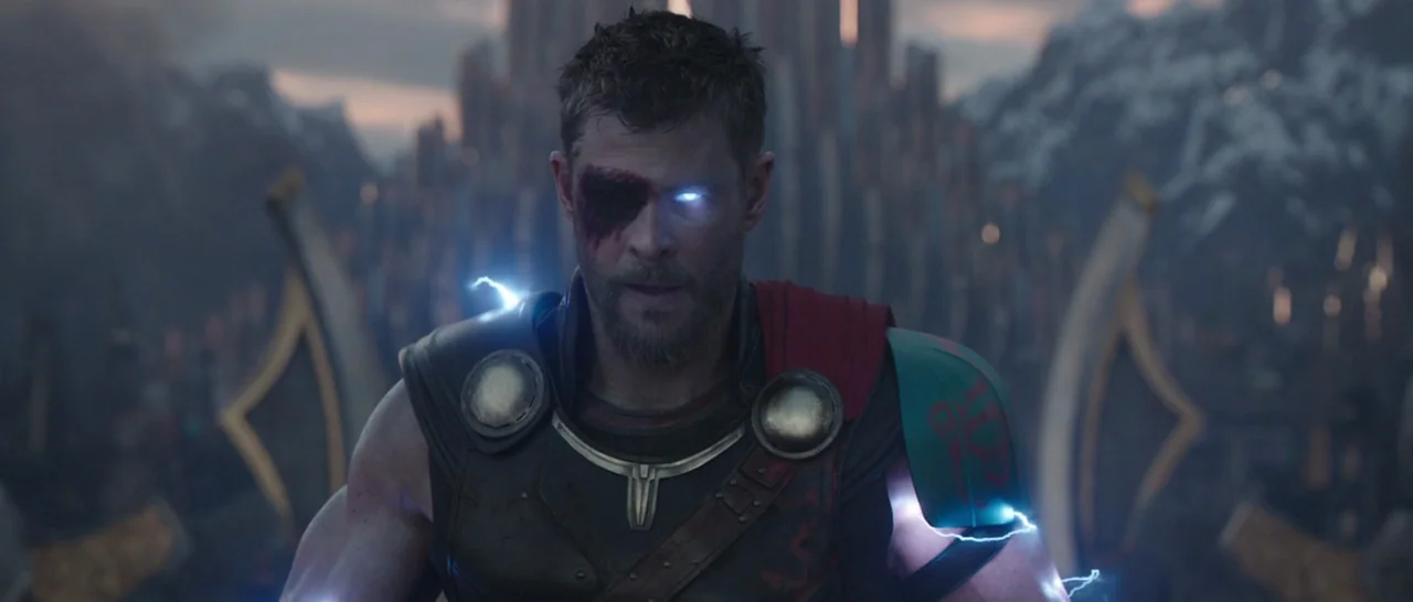 Thor: Ragnarok (2017) movie still: medium — A figure stands before a massive stone structure with layered spires under a dim sky. Electrical arcs…