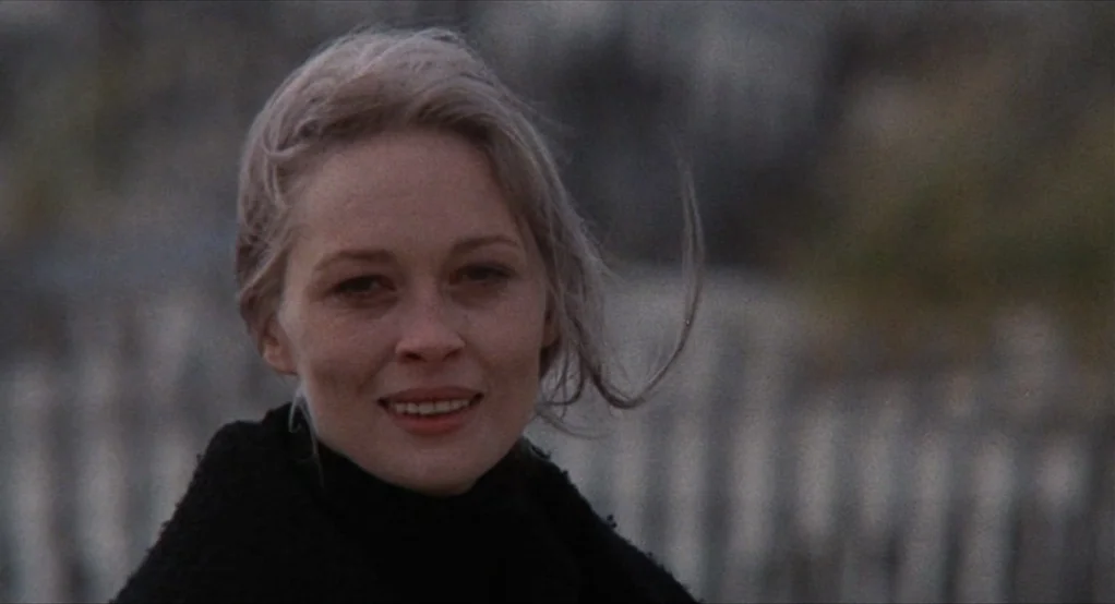 Puzzle of a Downfall Child (1970) movie still: closeup — A blonde woman stands outdoors with an out-of-focus wooden fence in the distance. The woman…
