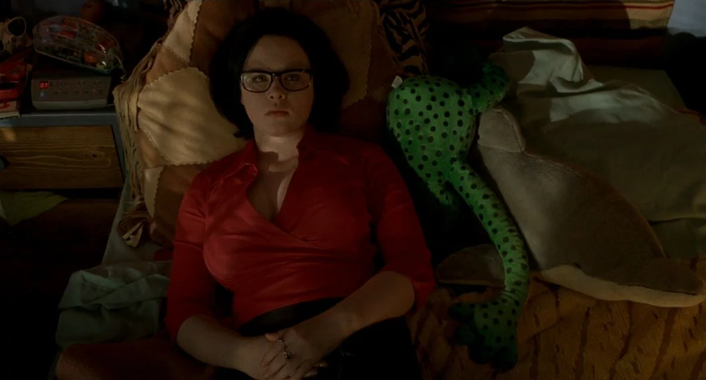 Ghost World (2001) movie still: medium — A cluttered bed with patterned pillows and stuffed animals occupies the foreground space. A woman in a red…