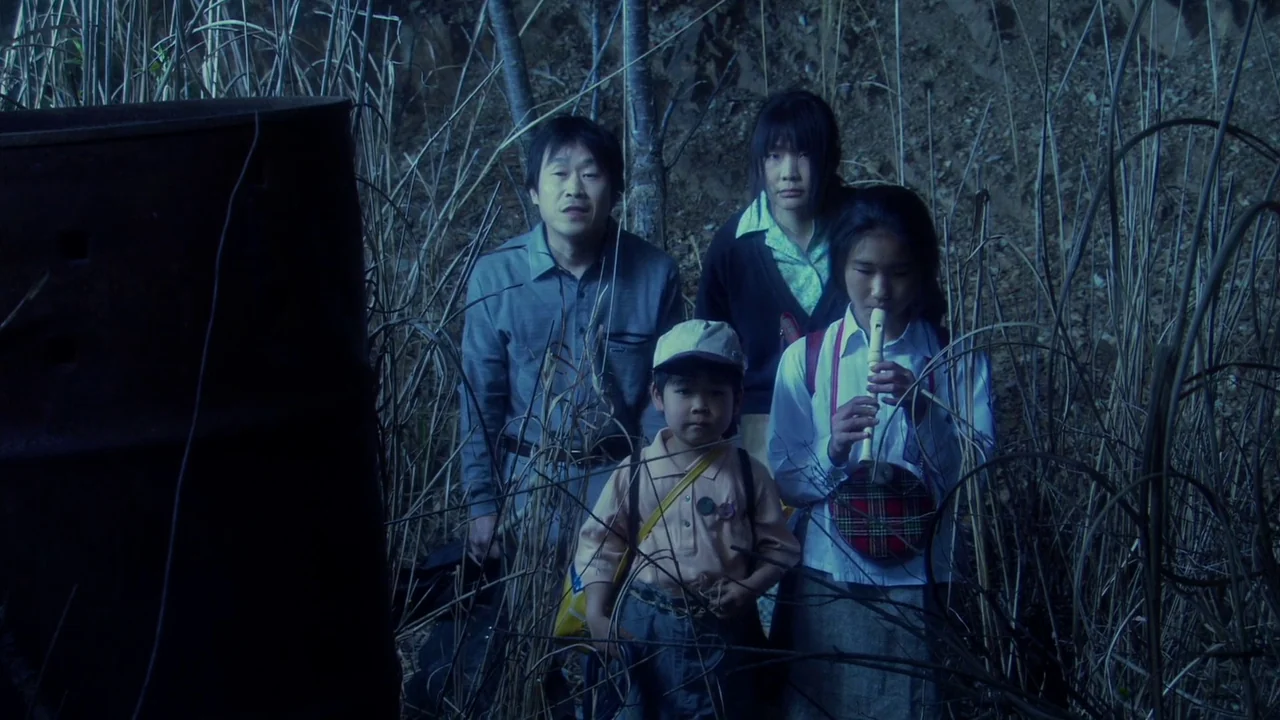 The Happiness of the Katakuris (2001) movie still: medium — Four people stand together in a patch of tall, dried stalks at night. They appear to be…