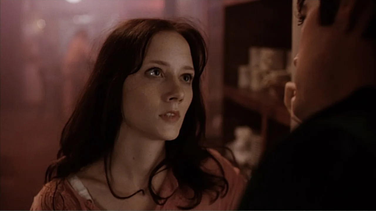 Against the Wall (1994) movie still: closeup — An interior retail space with dark shelves visible in the background and soft light. A young woman…