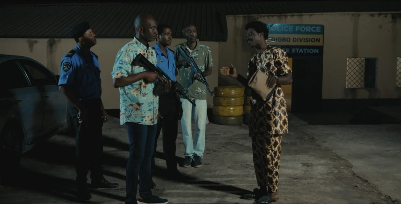 Project Assault (2025) movie still: fullbody — An asphalt yard outside a building with a blue sign identifies it as a division. Four men stand…