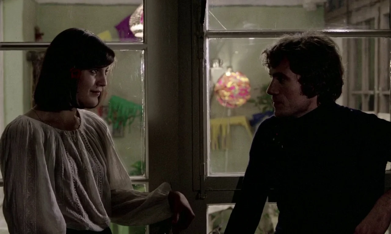 The Lost Honour of Katharina Blum (1975) movie still: medium — A man and a woman stand on opposite sides of a divided glass window. Decorated…