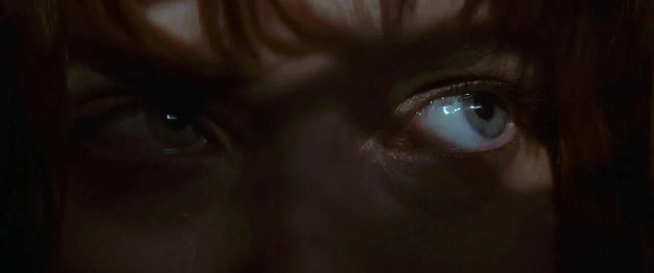 Elizabeth Harvest movie still: closeup — A close-up view of a person's eyes in a dark environment. The pupils and iris are illuminated while the…