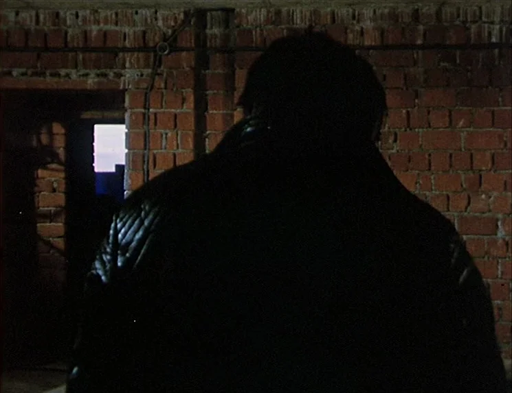 The Niklashausen Journey (1970) movie still: medium — A dark, unrefined space features unfinished red brick walls and visible conduit wiring. A lone…