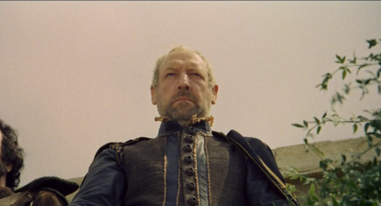 Beatrice Cenci (1969) movie still: medium — A stone fortification parapet sits against an overcast, pale sky. An older man in a blue period doublet…