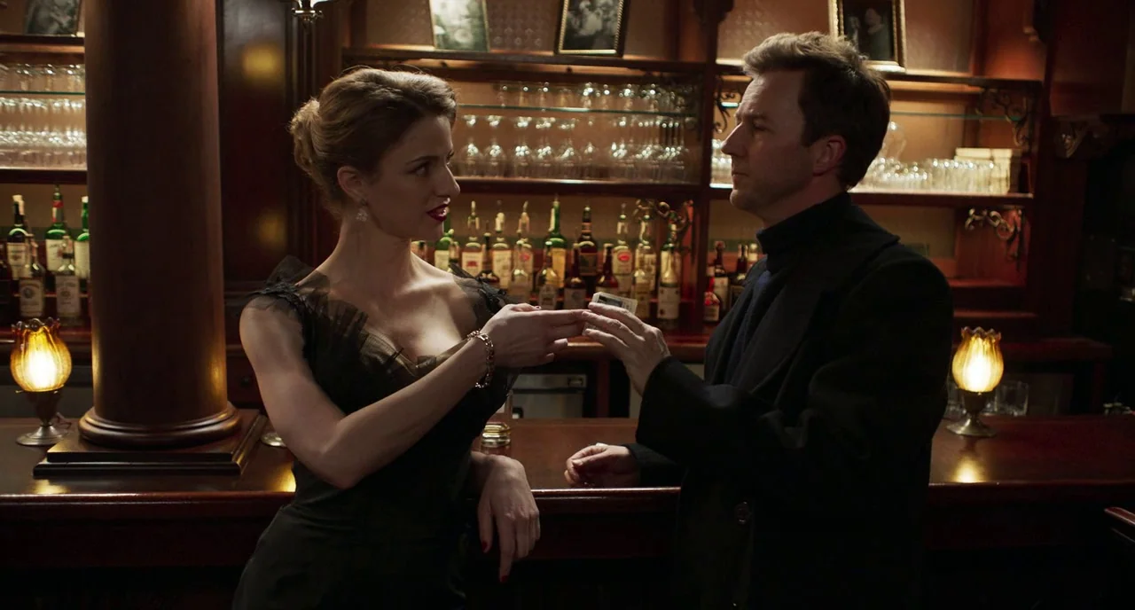Motherless Brooklyn (2019) movie still: medium — An dimly lit, traditional wooden bar features rows of bottles on shelves behind glass. A woman in a…