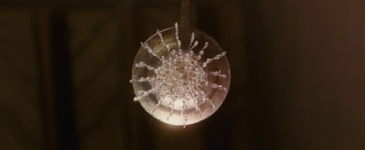 Hanna (2011) movie still: closeup — A circular metal showerhead is suspended against a dark, featureless background. Water droplets radiate outward…