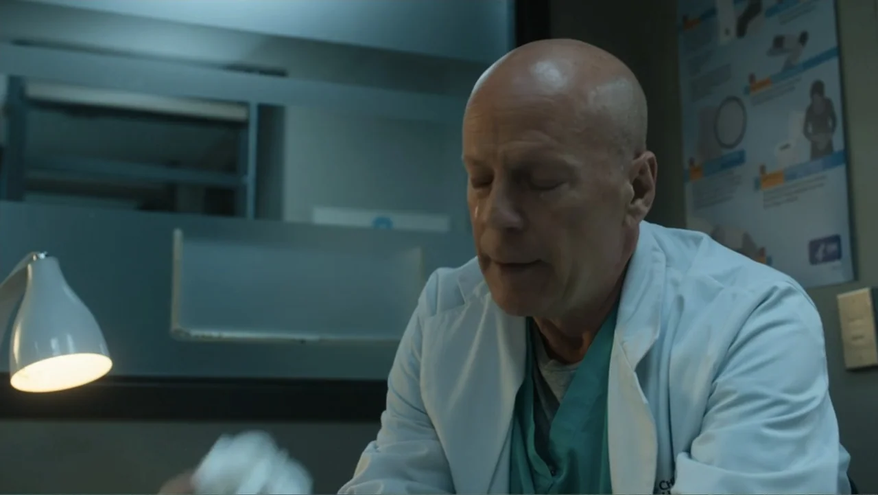 Death Wish (2018) movie still: medium — A dimly lit professional medical consultation room with a white desk lamp. A bald elderly man in a lab coat…