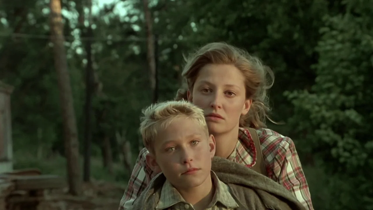Downfall (2004) movie still: medium — A woman and a young boy ride a bicycle through a wooded path. The background is composed of out-of-focus green…